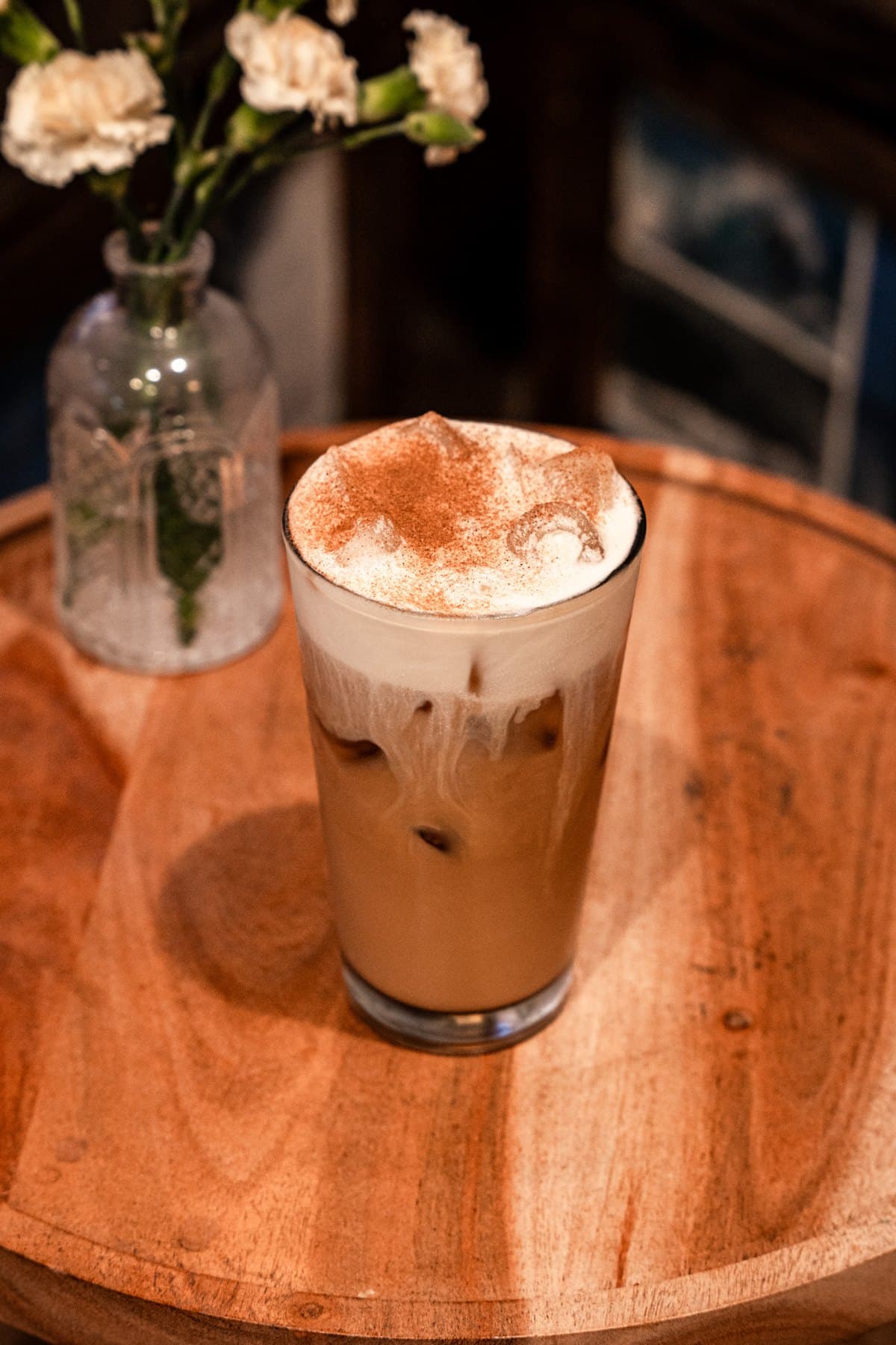 Iced Banana Maple Latte with cinnamon-dusted cold foam on a wood table